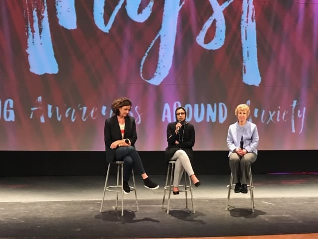Laura and 2 other panelists sitting on stools in front of screen onstage.
